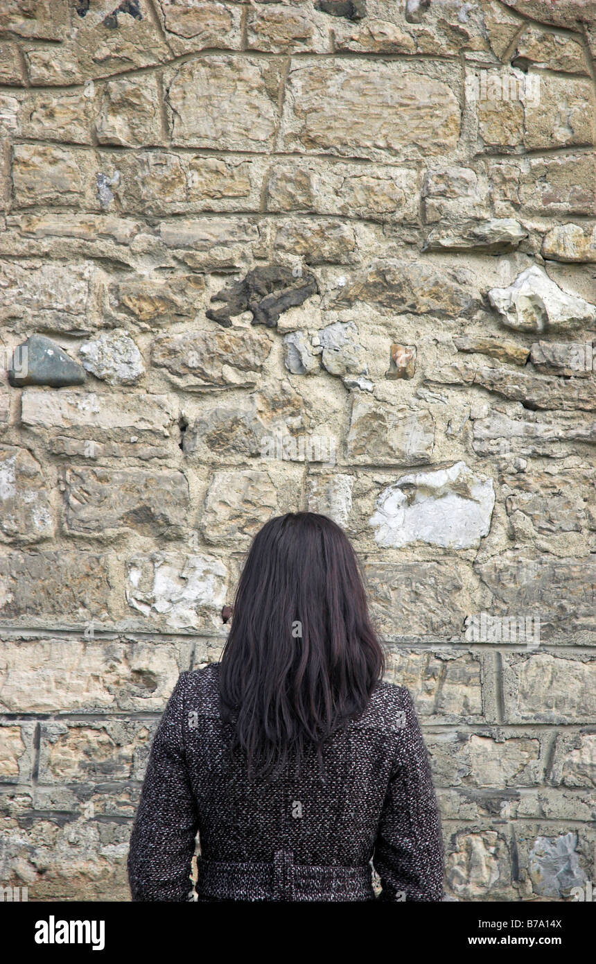 Mujer joven que se enfrenta a la pared de piedra Foto de stock