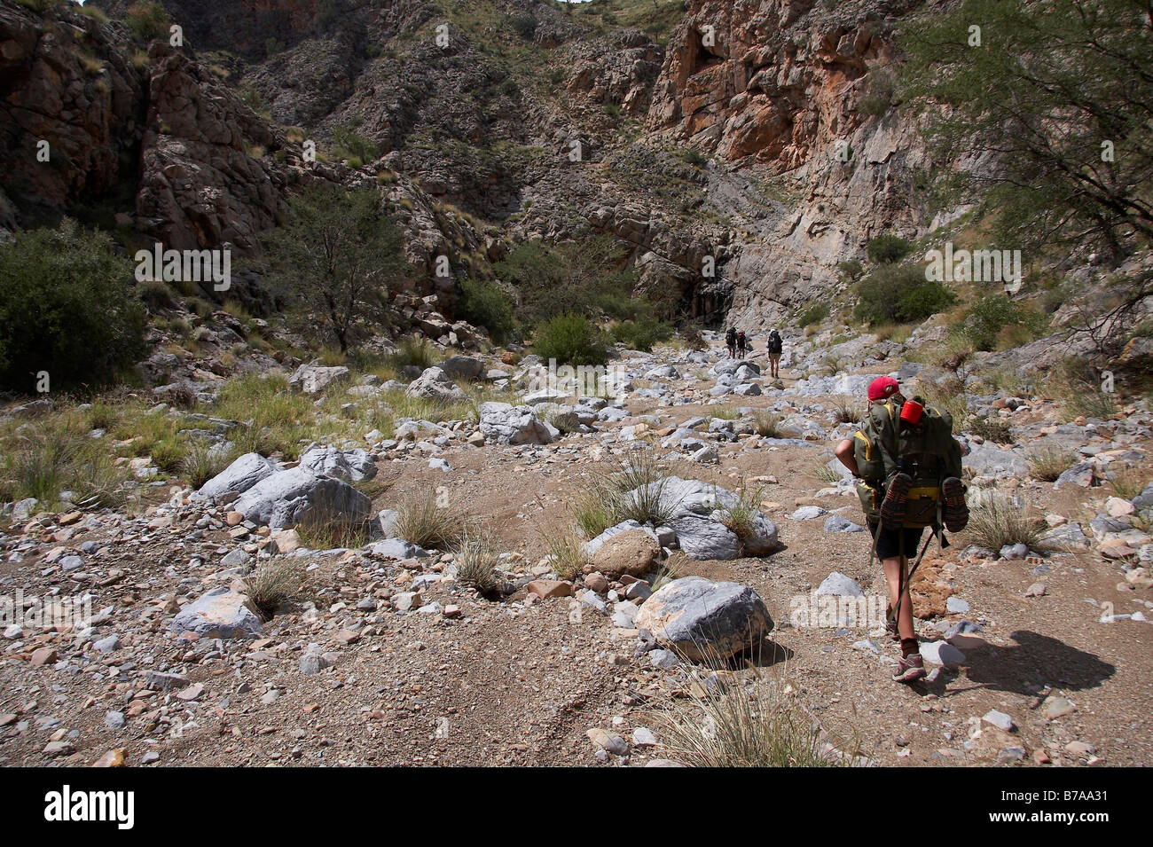 Un adolescente en una gorra roja caminando por un lecho de río salpicado de rocas en el Naukluft Hiking Trail Foto de stock
