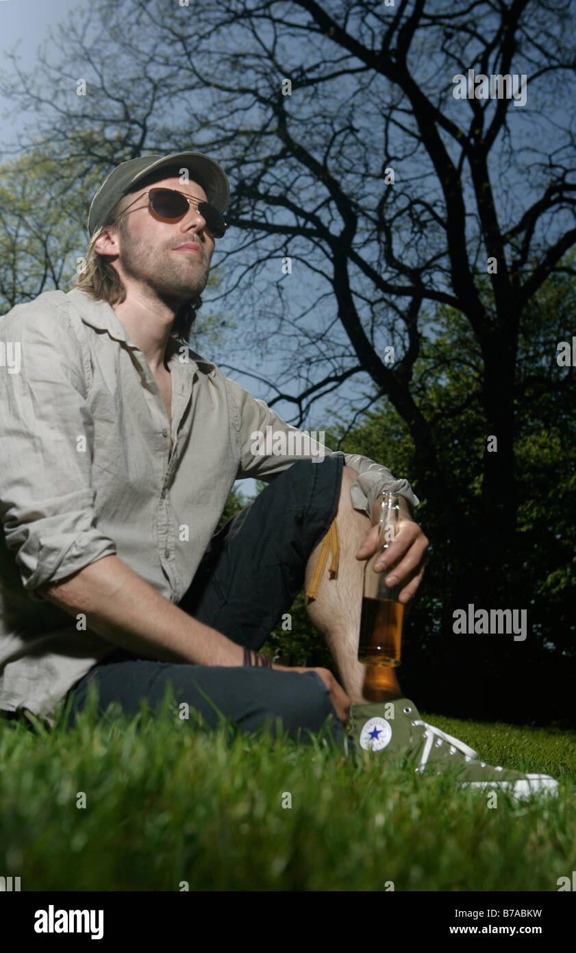 Joven sentado en un parque sosteniendo su bebida Foto de stock