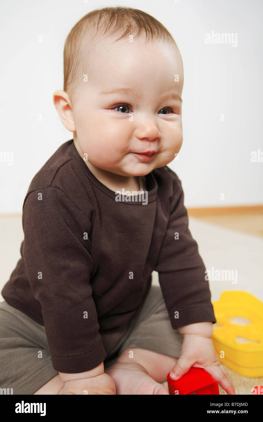 Bebé de 4 meses de edad sentado con los pies descalzos sobre una alfombra.  Juguetes en primer plano Fotografía de stock - Alamy