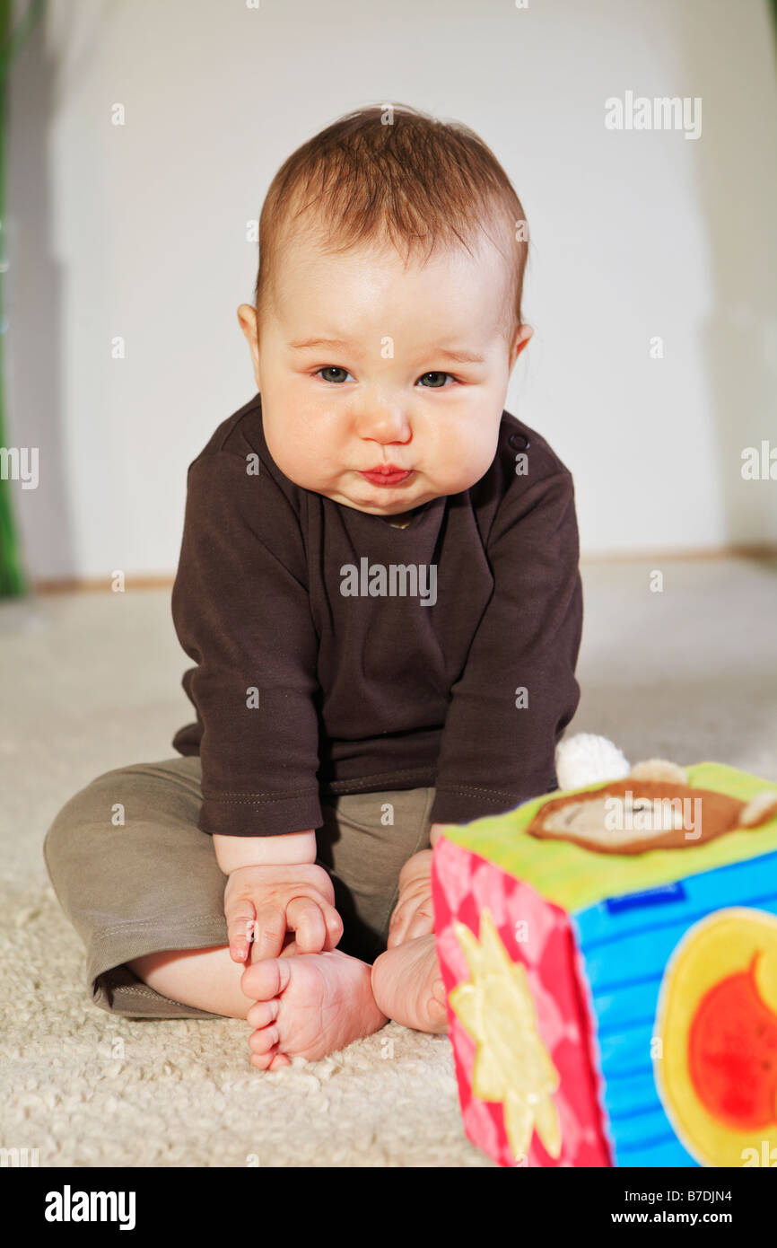 Bebé de 4 meses de edad sentado con los pies descalzos sobre una alfombra.  Juguetes en primer plano Fotografía de stock - Alamy