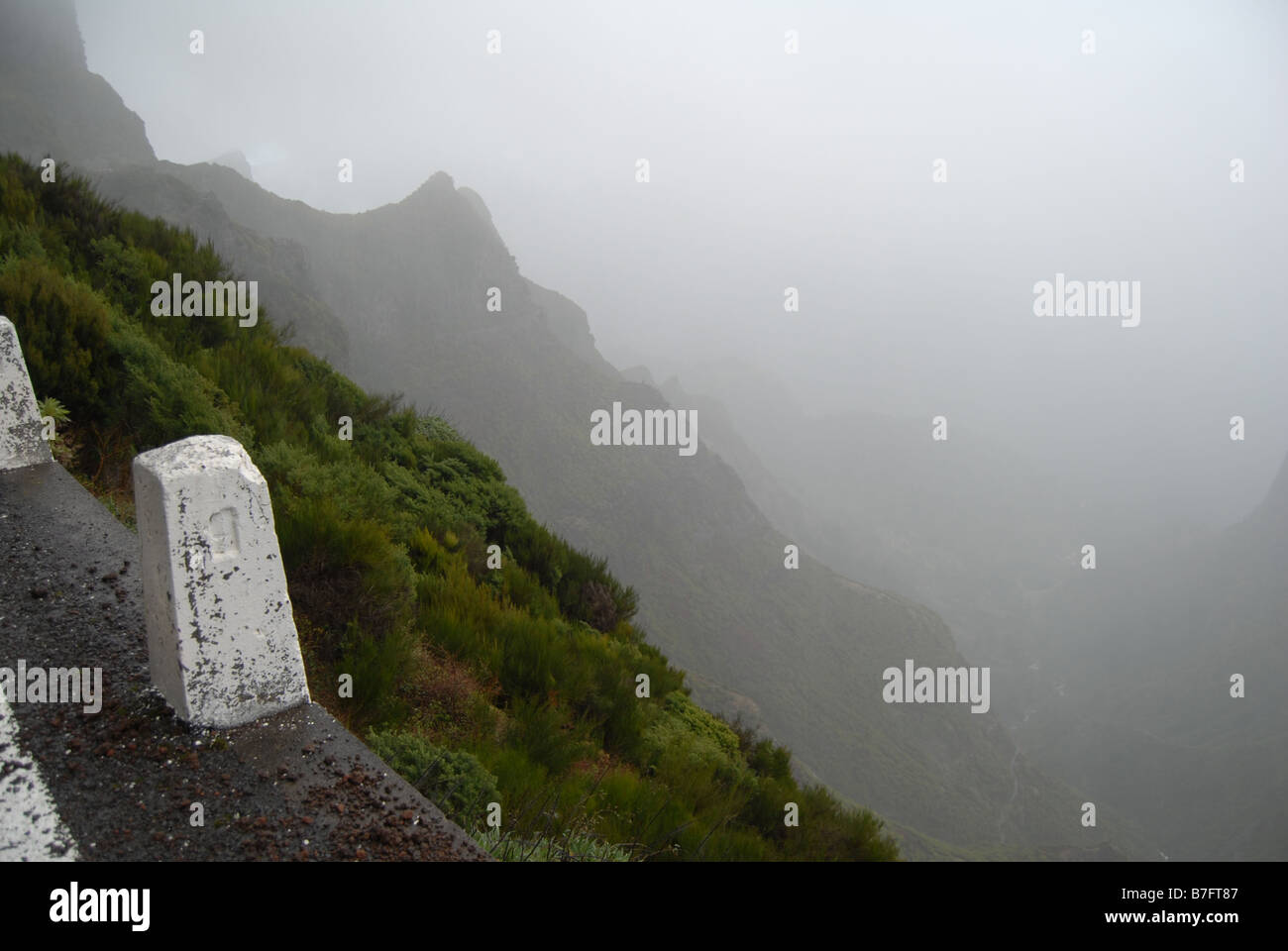Un Misty escena con acantilados dentados en el fondo y el borde de una carretera en primer plano , Madeira , Portugal Foto de stock