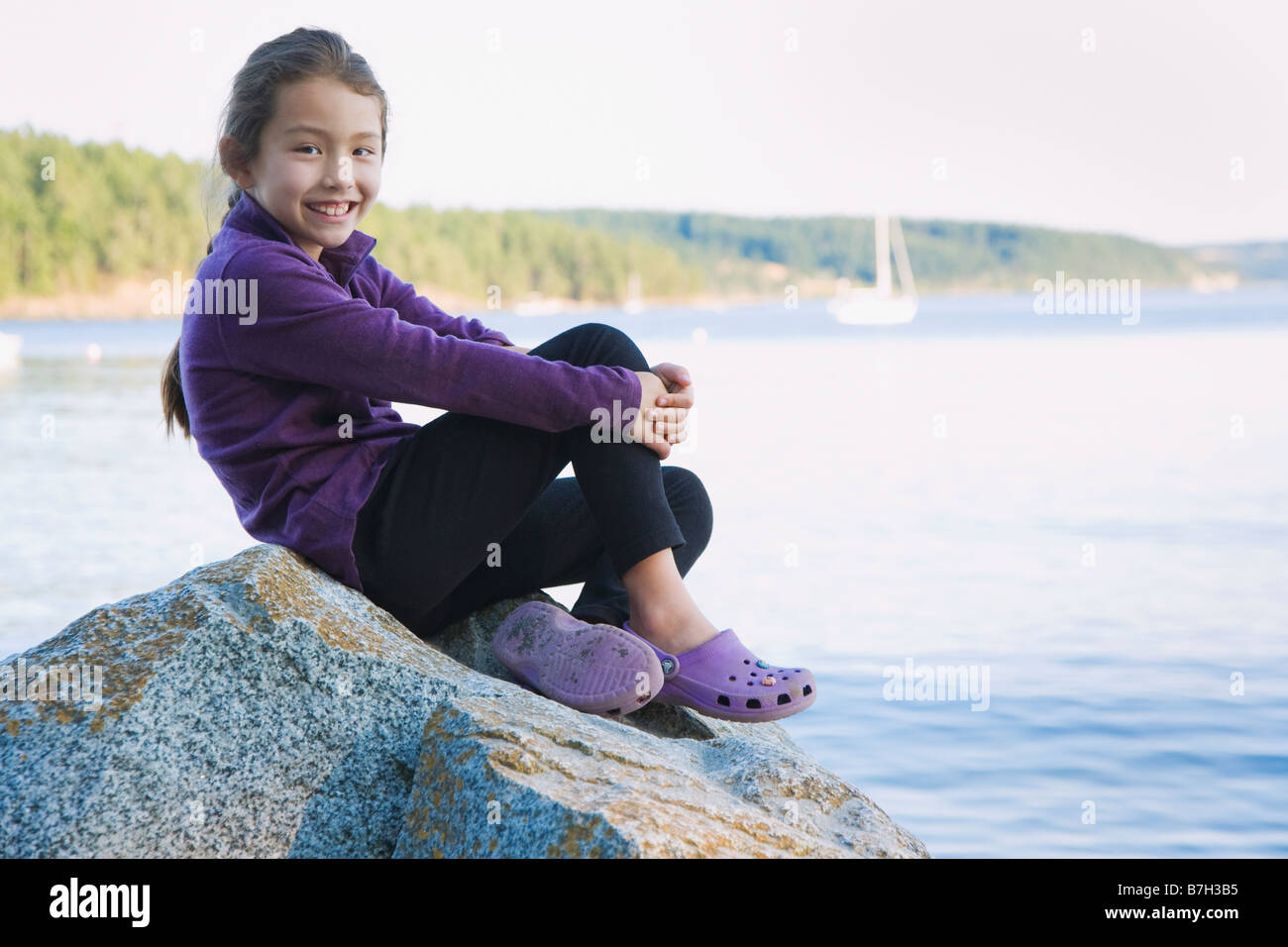Asian chica sentada en la orilla rocosa Foto de stock