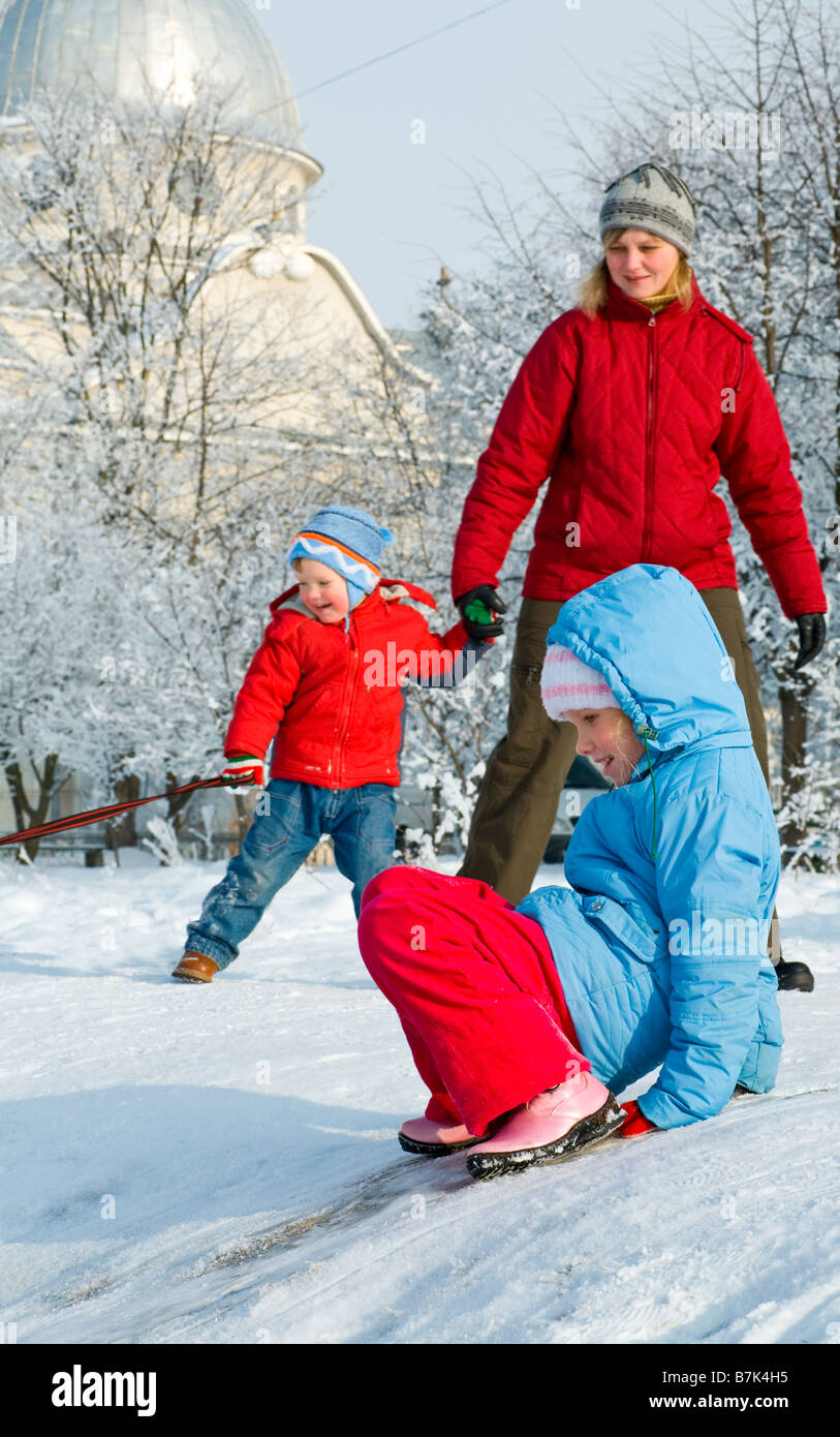 (Madre de familia feliz con pequeño chico y chica) en invierno patio cubierto de nieve cerca de casa Foto de stock