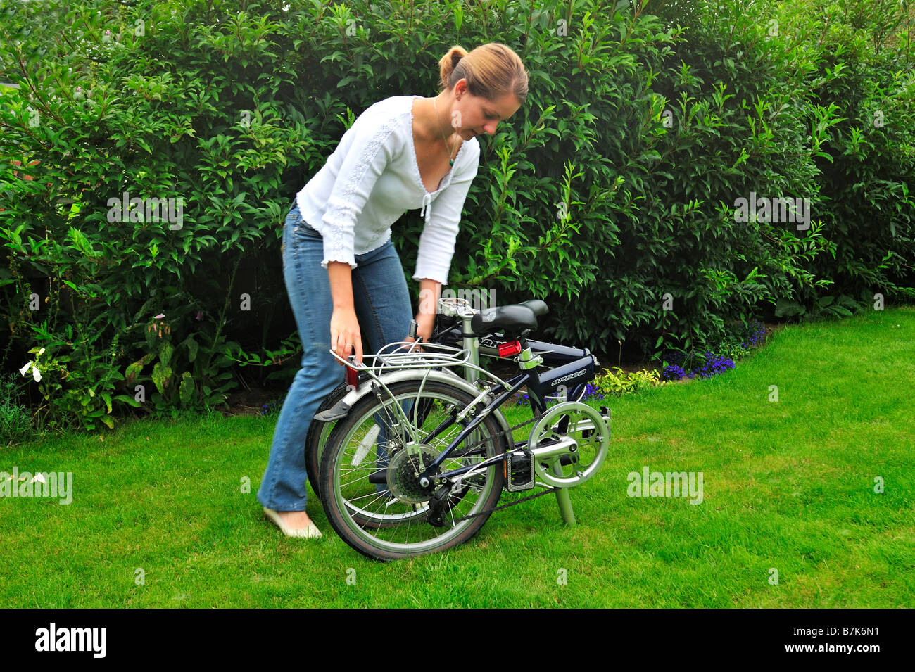 Una joven en el proceso de plegado de una bicicleta plegable. Ligero desenfoque de movimiento en sus manos. Foto de stock