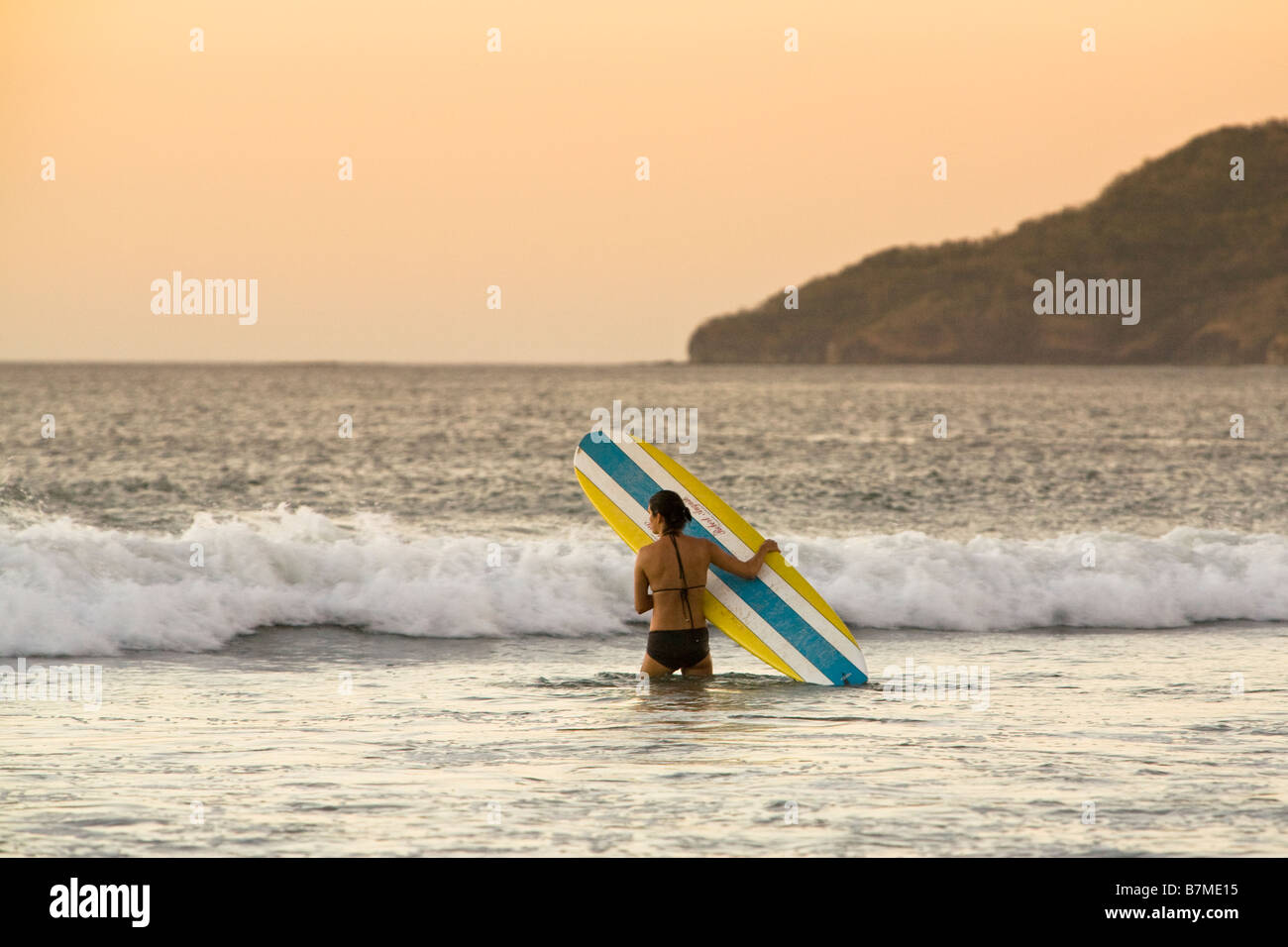 Surfer celebración surfboard entrando en las olas de la Playa Tamarindo, Costa Rica. Foto de stock