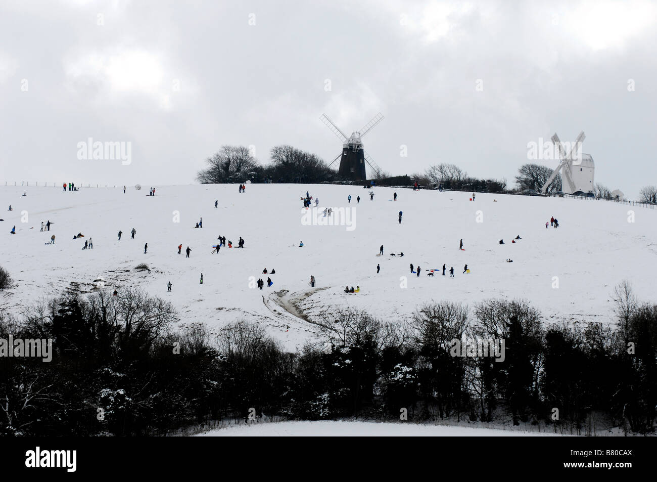Las figuras que salpican la ladera como una pintura Lowry mientras disfrutan de la nieve en el Jack y Jill molinos en Clayton Sussex, UK Foto de stock