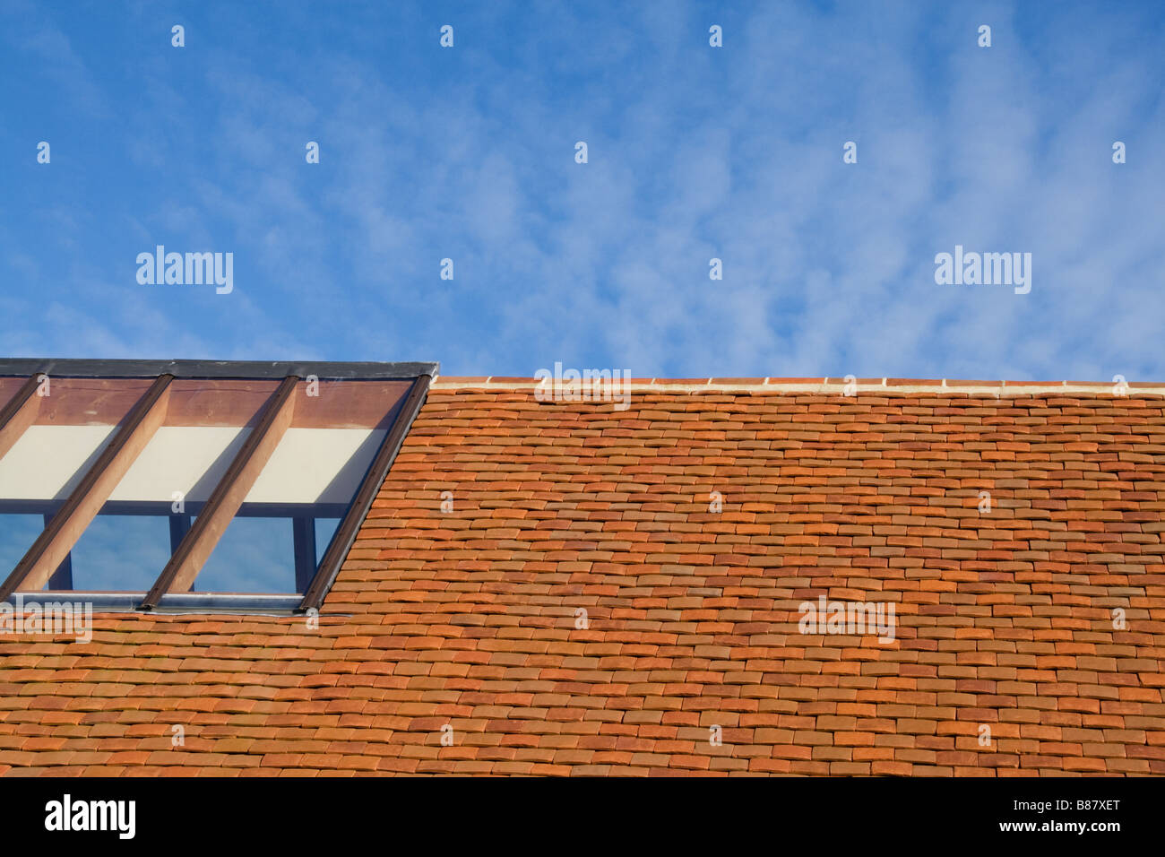 Techo de tejas de arcilla roja, contra un cielo azul, con un techo de vidrio claro. Foto de stock