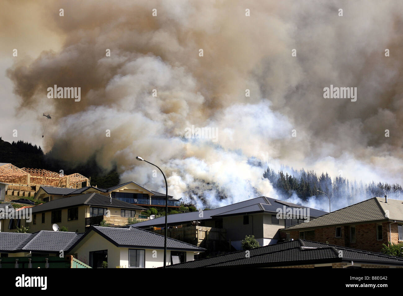 Helicópteros con baldes de monzón luchando contra un incendio asola bosque cercano a propiedades en Nueva Zelanda Foto de stock