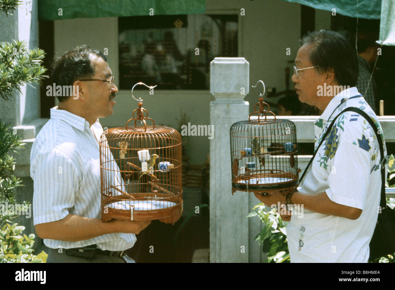 Dos hombres que ocupan birdcages canción que contenga las aves en el mercado de pájaros de Mongkok de Yuen Po Street, Kowloon, Hong Kong Foto de stock