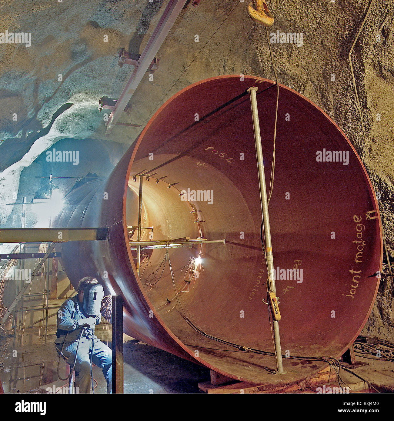 Ingeniero de soldadura de acero de un enorme tubo de ventilación en un túnel de transporte suizo, a través de arduas excavayed roca volcánica. Foto de stock