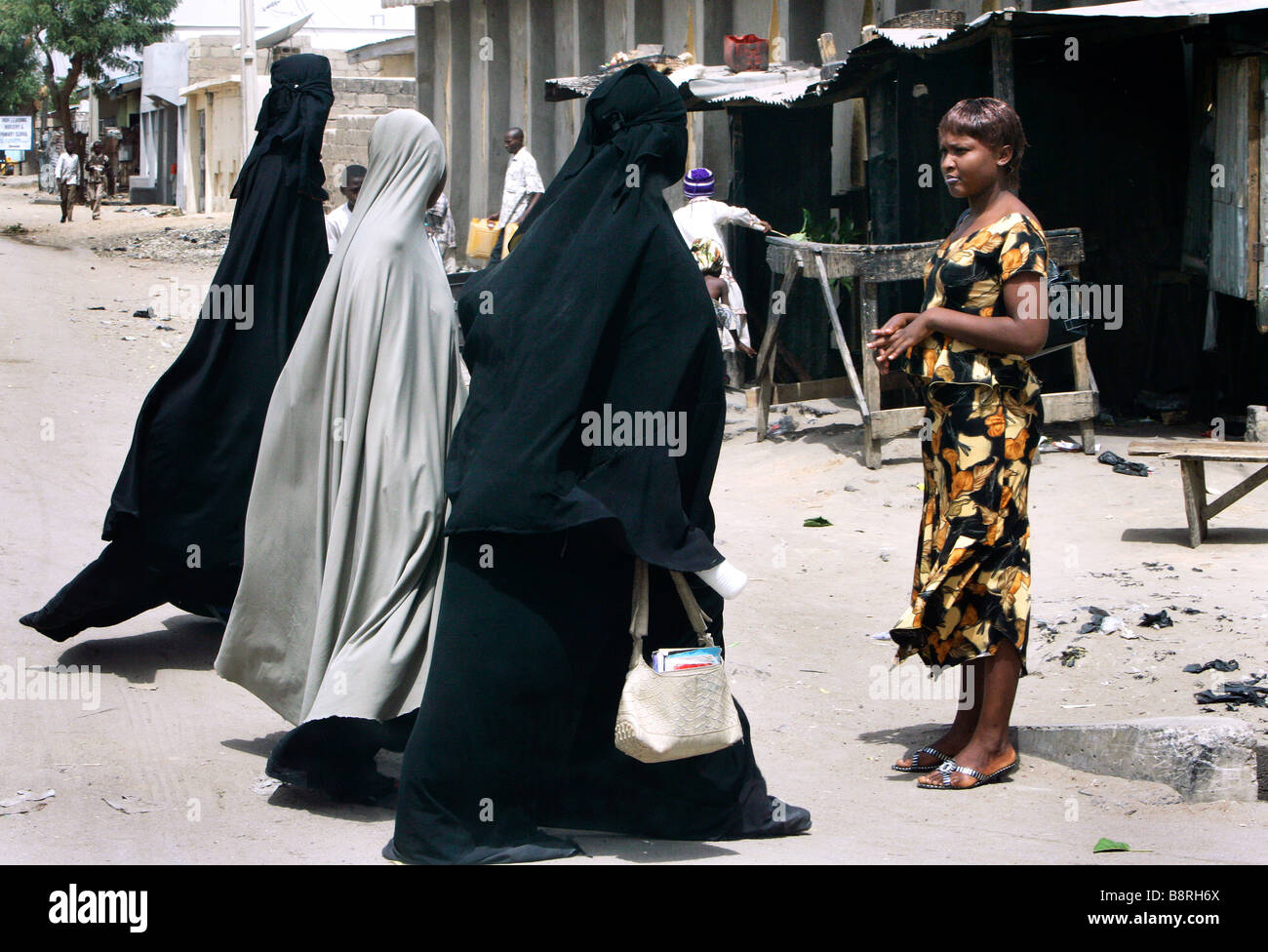 Un escéptico moderno busca vestidos mujer cristiana mirando a mujeres musulmanas llevando una burka de cuerpo completo. Estado de Borno, Maiduguri, Nigeria Foto de stock