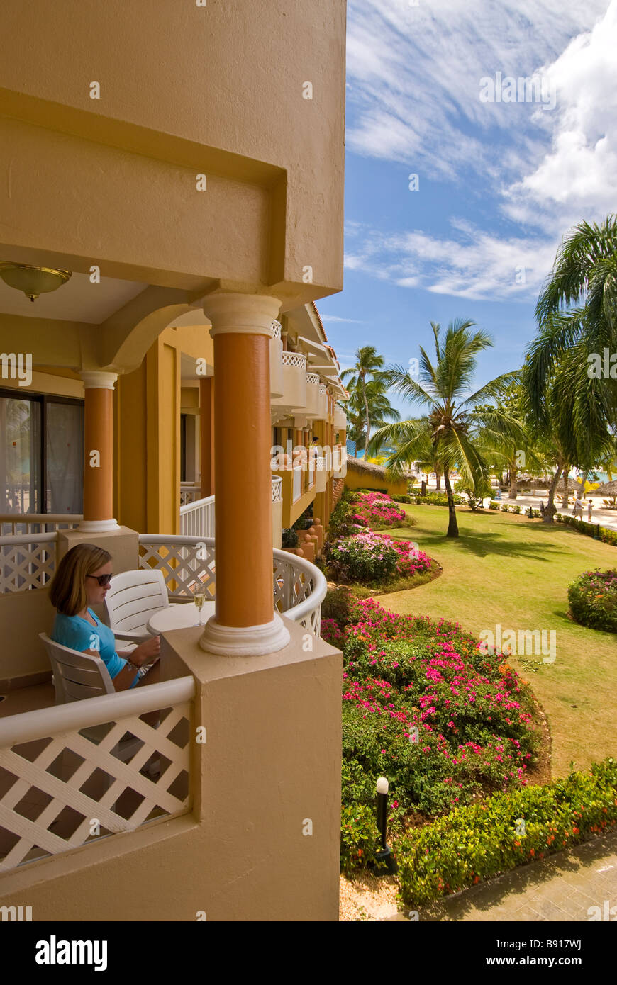 Mujer sentada en el balcón del hotel Bayahibe Viva Wyndham Dominicus Palace resort all-inclusive con palmeras República Dominicana Foto de stock