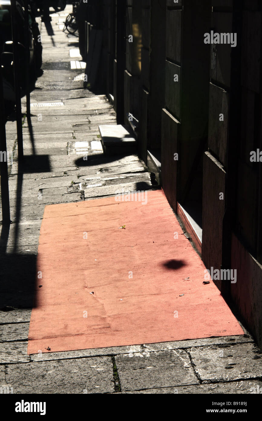 Una vieja y sucia alfombra roja fuera de tienda en vacante vacía acera en la ciudad de sun Foto de stock