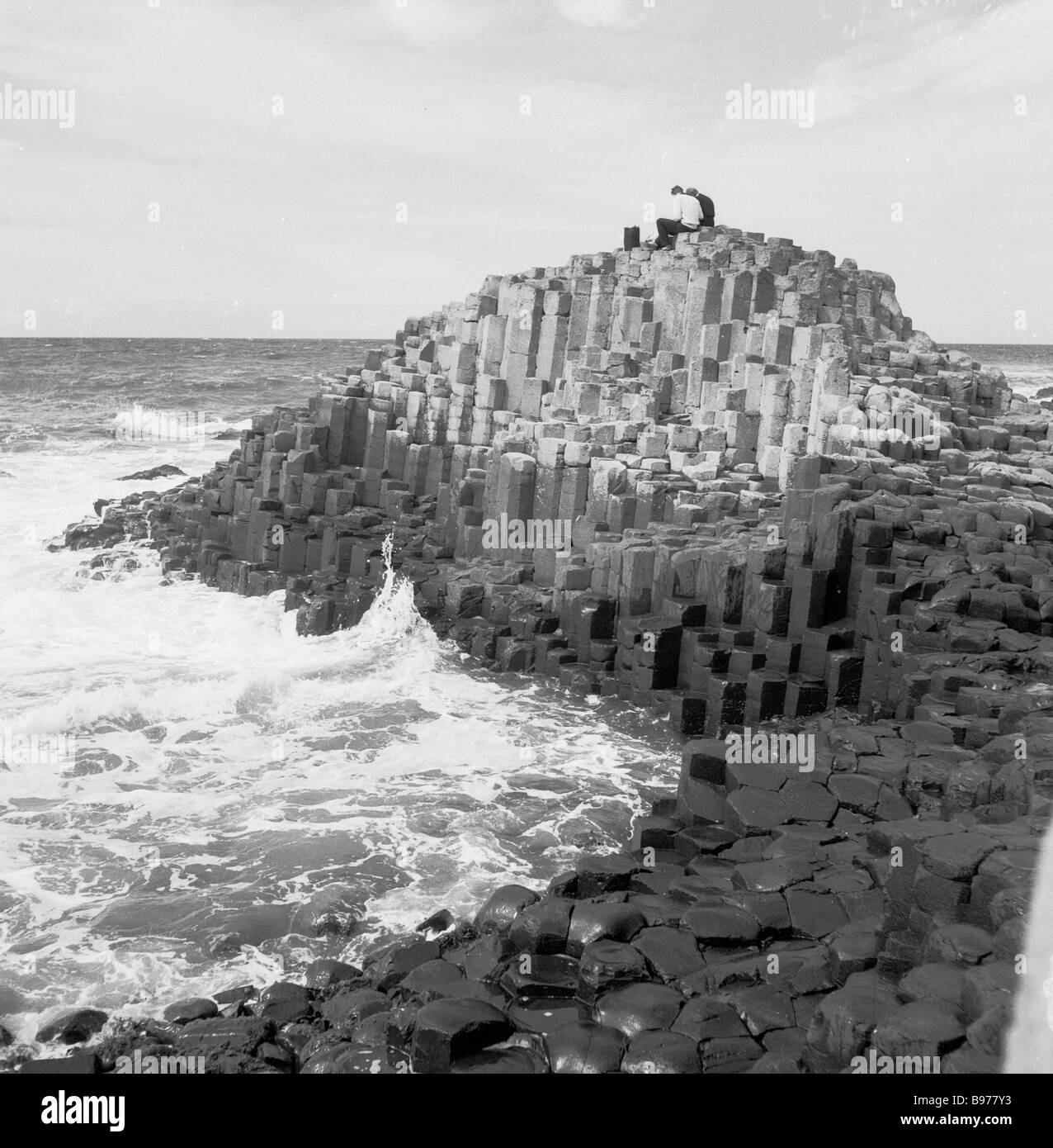 1950s, histórico, los visitantes se sientan en las antiguas formaciones rocosas volcánicas, las columnas de basalto, en la famosa Calzada del Gigante, Antrim, Irlanda del Norte. Foto de stock