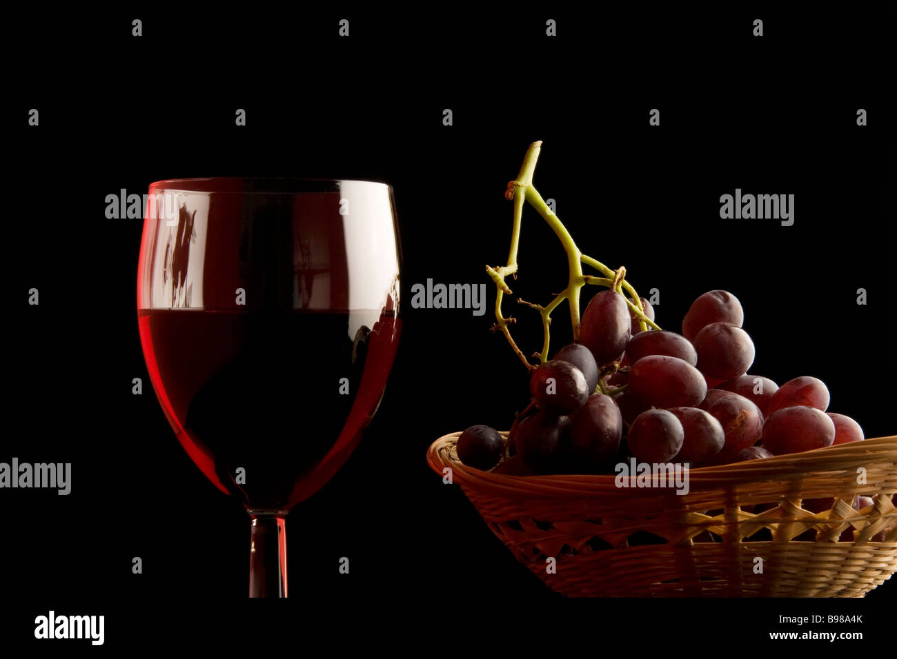 Un vaso de vino tinto y una cesta de uvas rojas. Foto de stock