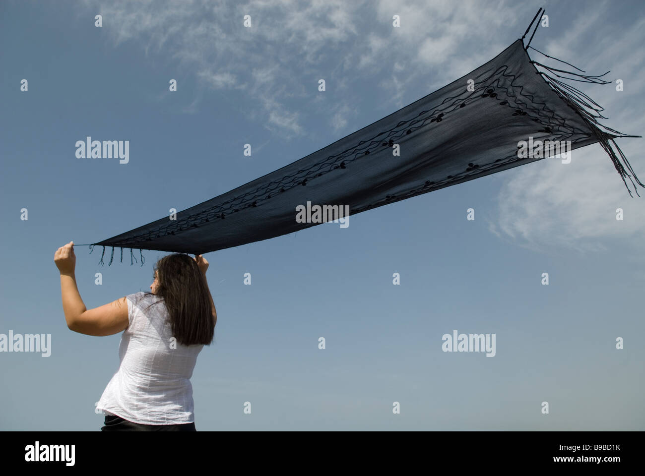 Mujer saludando con un pañuelo negro contra un cielo azul Foto de stock
