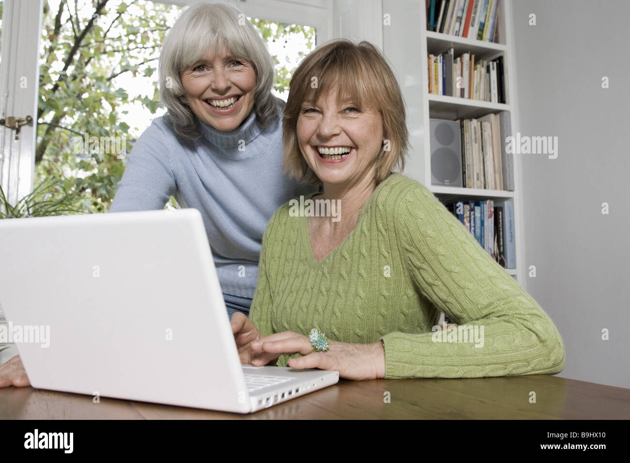 Entrada de datos portátil ancianos risas detalle series personas mayores mujer alegremente dos equipos de procesamiento de datos al navegar por internet Foto de stock