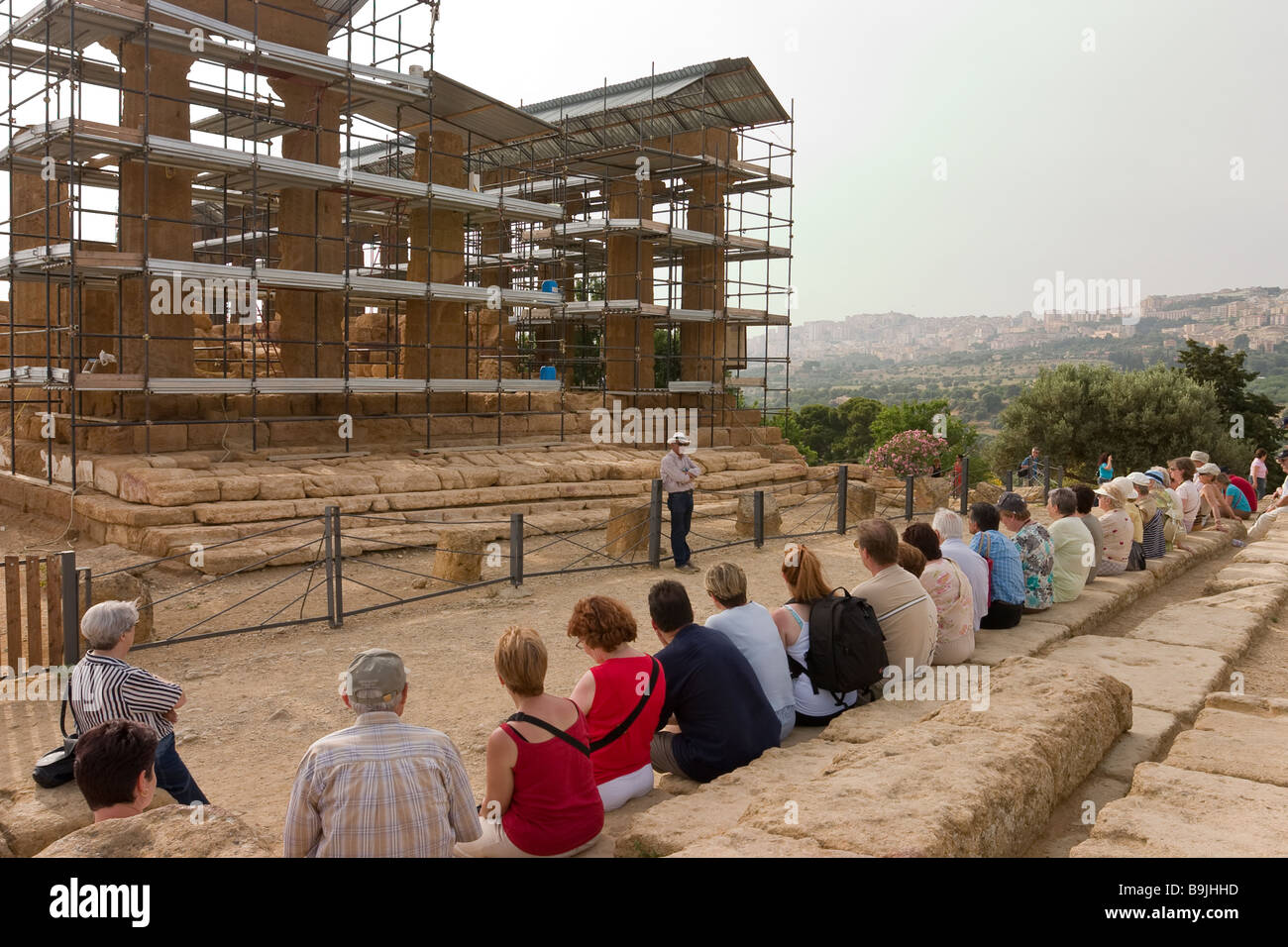Tour de charla. Un grupo de turistas se asienta sobre los antiguos pasos delante del templo de Juno Lacinia, que se describe en la guía. Foto de stock