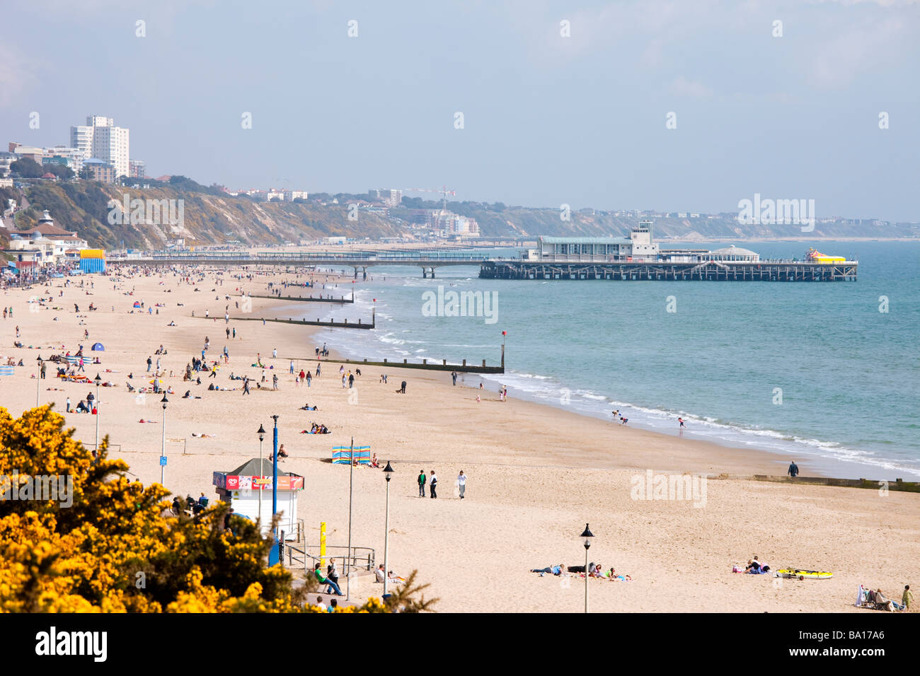 Muelle de Bournemouth y playa de arena dorada con hoteles en distancia y gente tomando sol con el cielo azul, el mar y los acantilados Foto de stock
