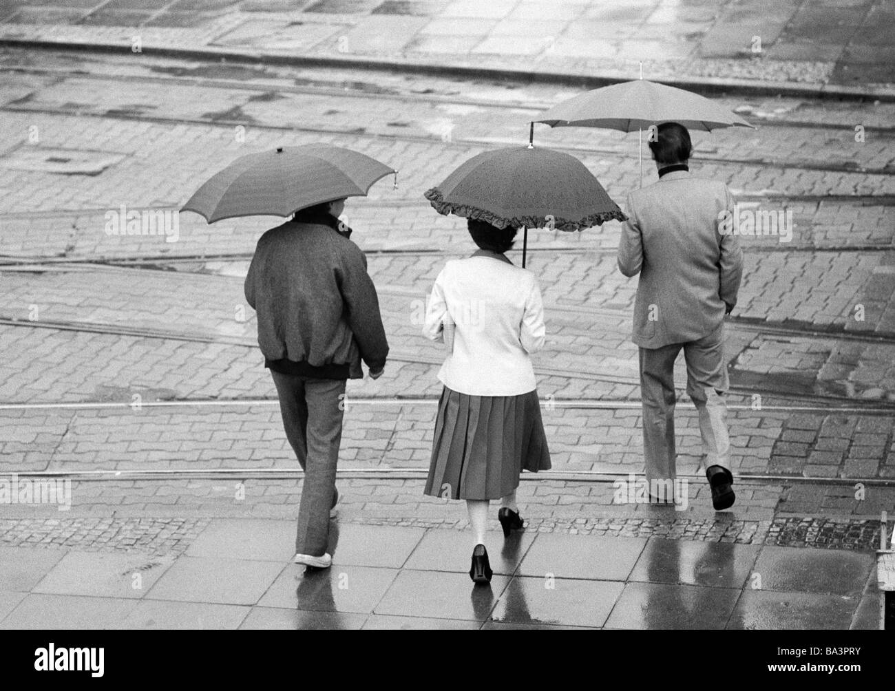 80, fotografía en blanco y negro, la familia se compromete a caminar bajo la lluvia, paraguas, hombre, de edades entre 40 y 50 años, mujer, con edades de 30 a 40 años, niño, a la edad de 14 a 16 años Foto de stock