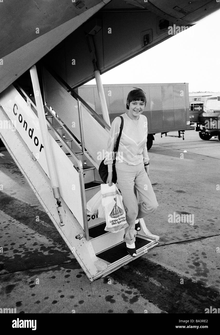 80, fotografía en blanco y negro, gente joven que deja un avión utilizando  el pasillo, pulli, pantalones, bolsos, bolsas de plástico con productos de  la tienda de duty-free, Condor, equipaje de mano,