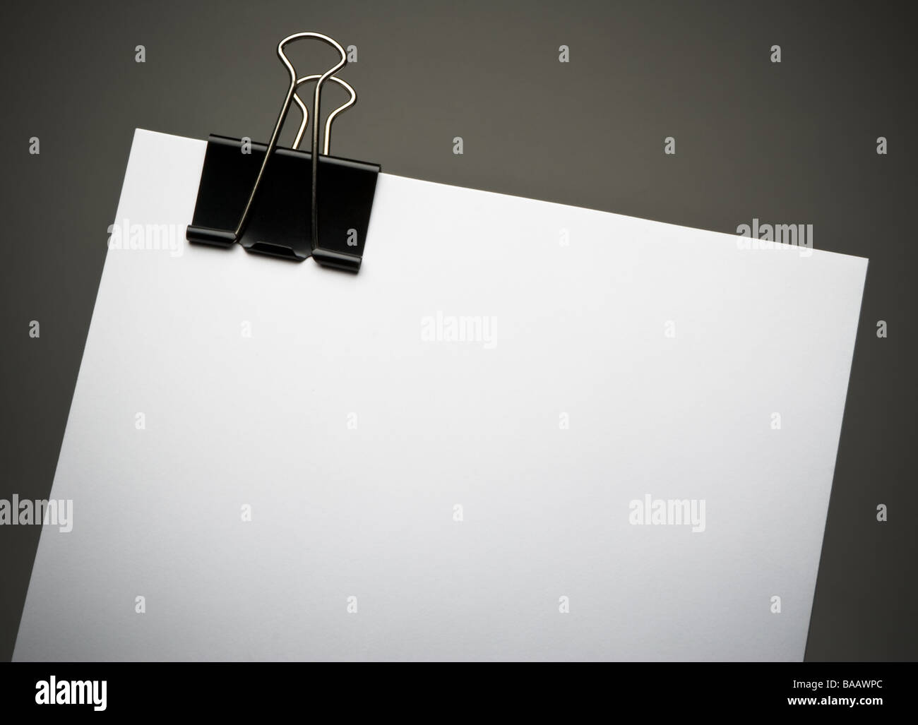 Papel blanco con negro grande clip binder en el borde superior, contra el fondo gris oscuro con sombra, Vignette composición horizontal Foto de stock