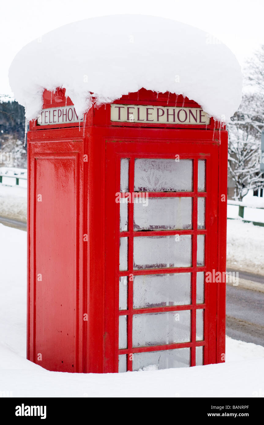 Un teléfono rojo cuadro en nieve profunda por la carretera en la aldea de Crathie, fuera el castillo de Balmoral, en las Tierras Altas de Escocia. Foto de stock