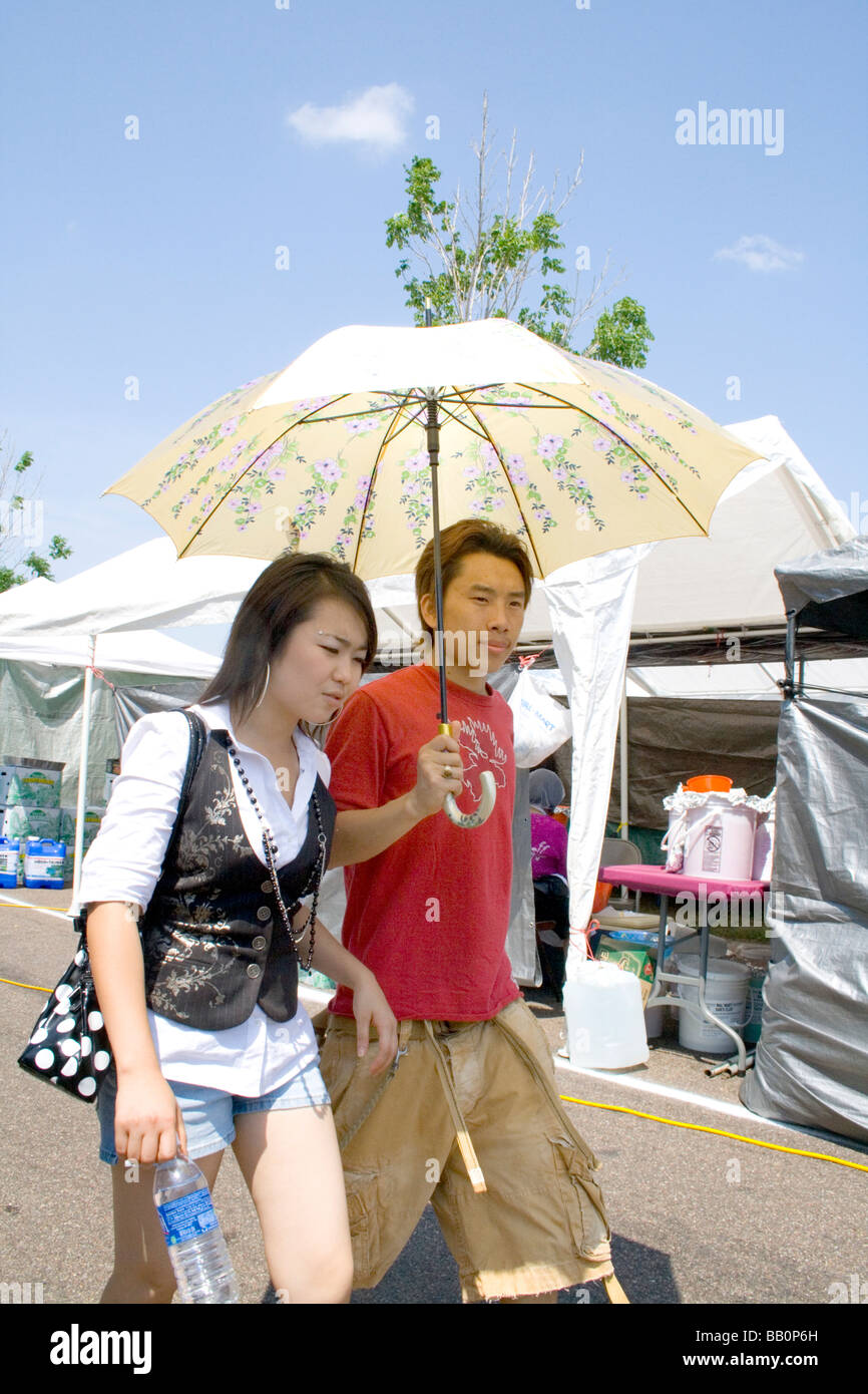 Pareja de adolescentes caminando bajo paraguas para proteger de los rayos  del sol. Festival de Deportes de Hmong McMurray campo St Paul Minnesota,  EE.UU Fotografía de stock - Alamy
