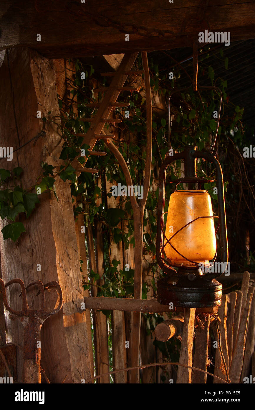 Detalle de un viejo granero en Francia con una lámpara de aceite oxidado y rastrillos y horquillas apilados contra la pared. Foto de stock
