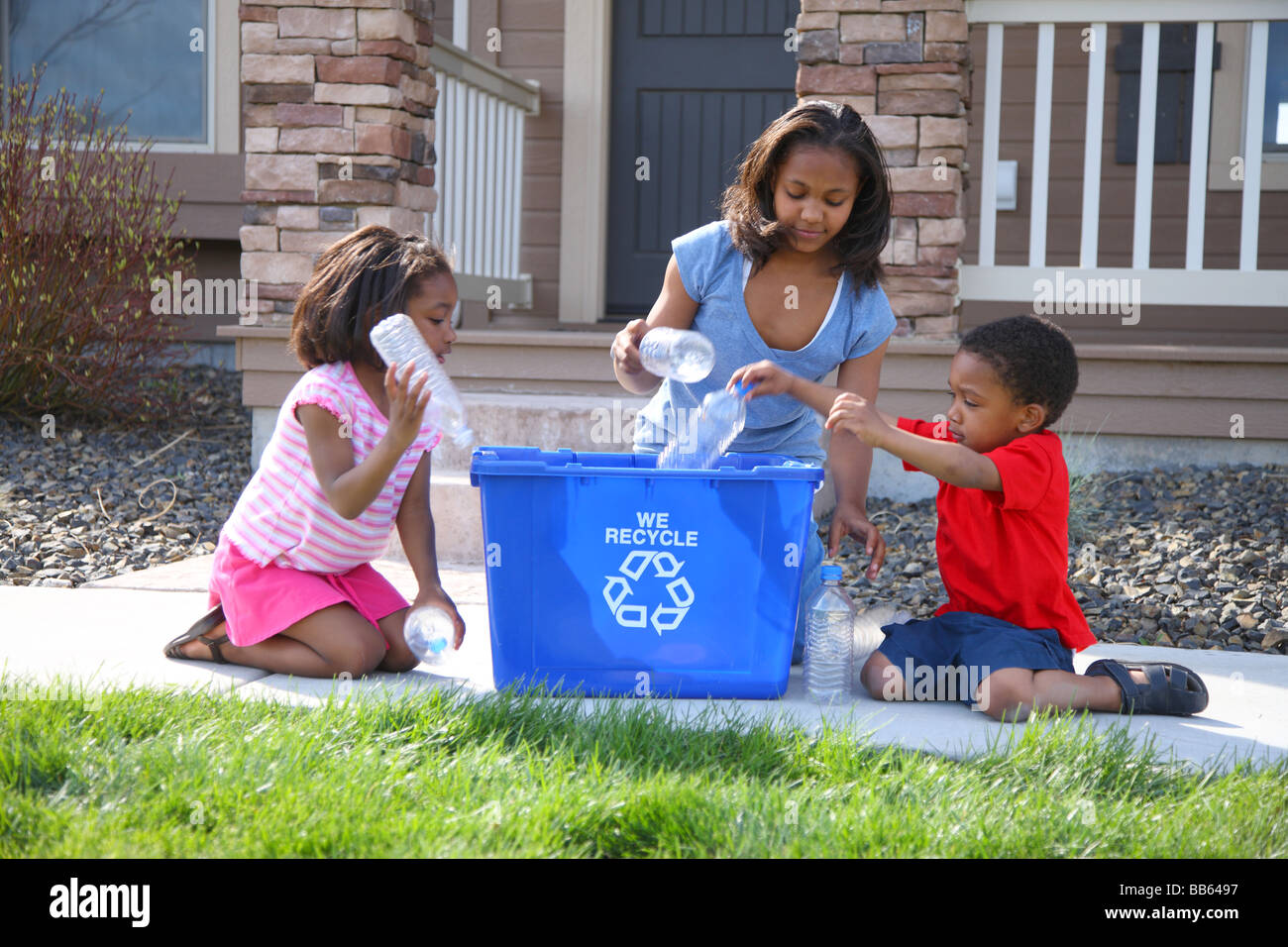 Tres niños colocando elementos en la papelera de reciclaje Foto de stock