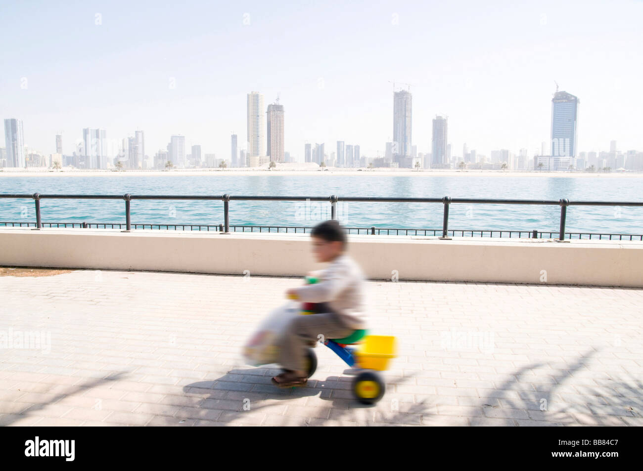 Niño en el tricyle frente a los rascacielos con movimiento desenfocado, Dubai, Emiratos Árabes Unidos Foto de stock