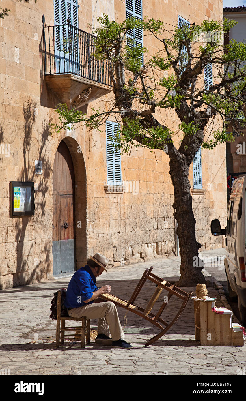 Hombre tejiendo en una silla de tapicería de rafia en calle Llucmajor Mallorca España Foto de stock