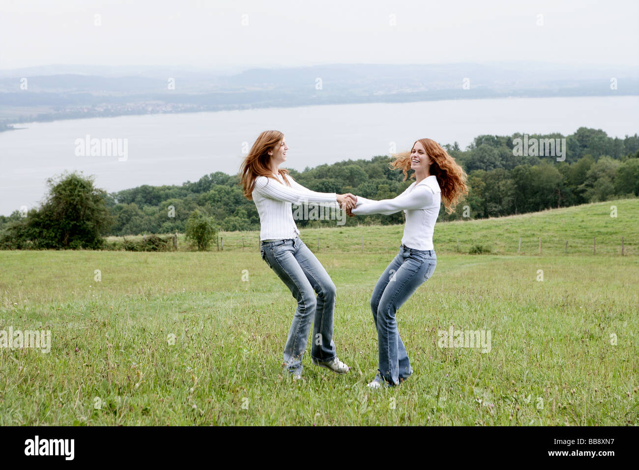 Dos adolescentes bailando en un campo con vista al lago Foto de stock