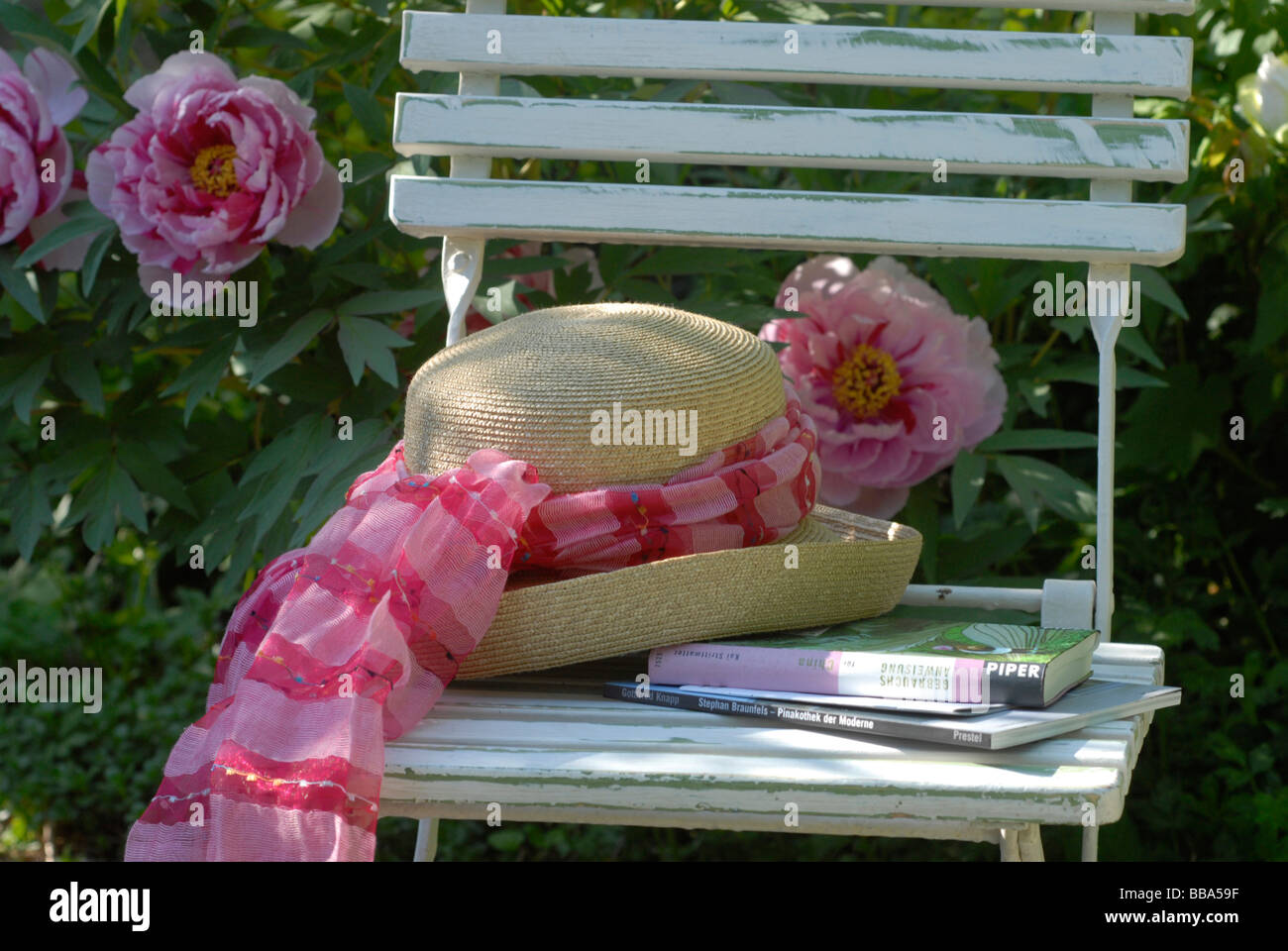 Sombrero en silla de jardín en la parte delantera de peonías Foto de stock