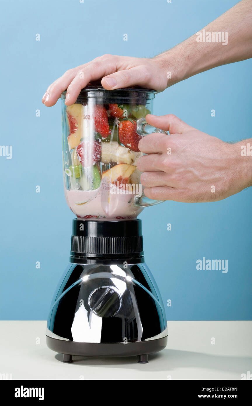 Una mano humana sosteniendo la batidora mientras mezclas de frutas  Fotografía de stock - Alamy