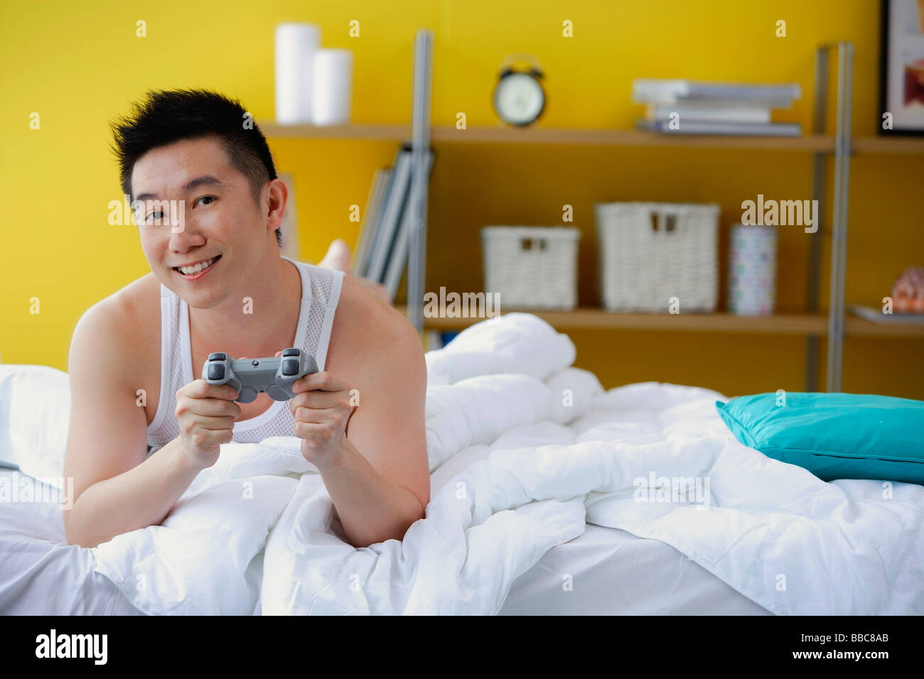 Hombre tumbado en la cama, manteniendo el control de videojuegos Foto de stock