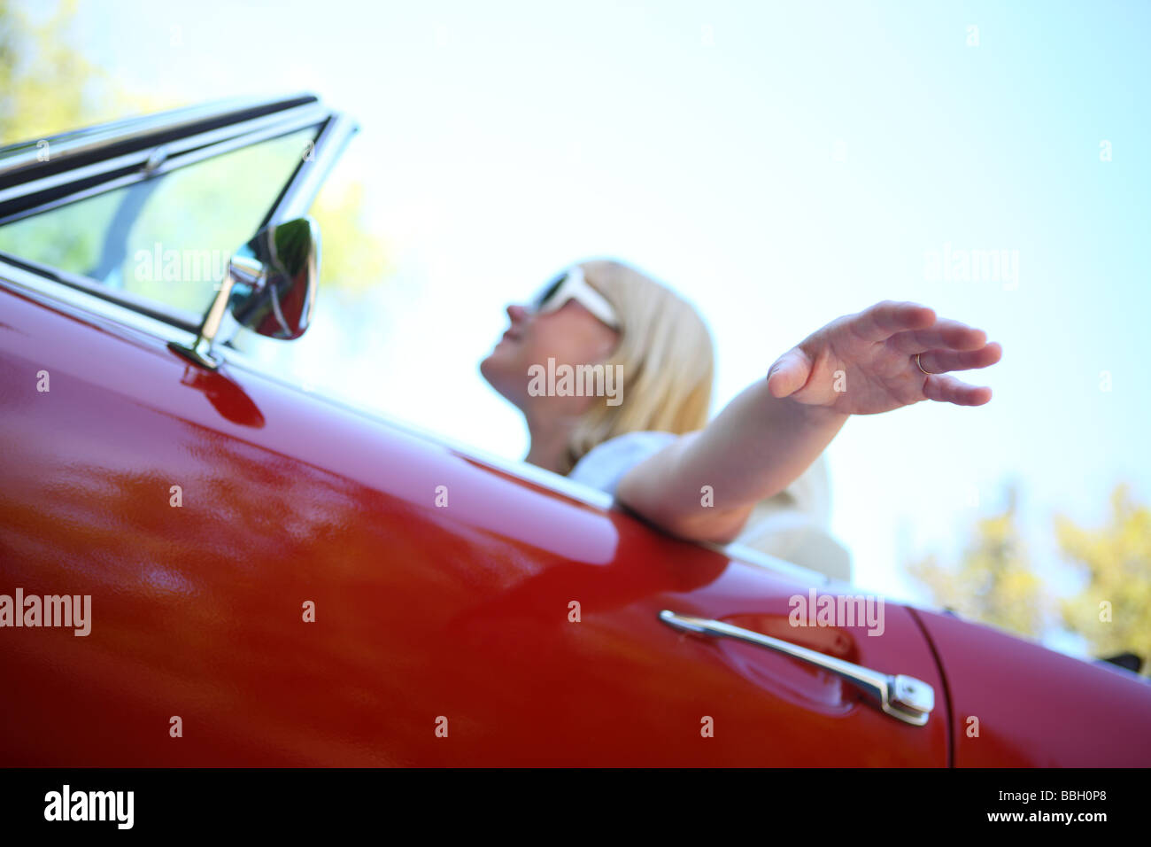 Mujer con la mano en el viento conduciendo un coche convertible Foto de stock