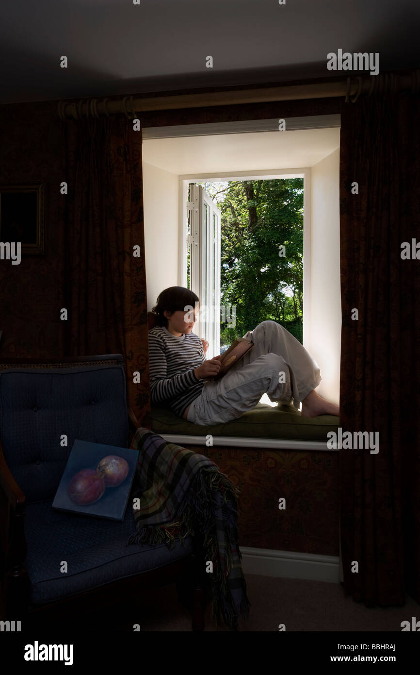 Hijo sentado en la ventana ope,lectura,casa Foto de stock