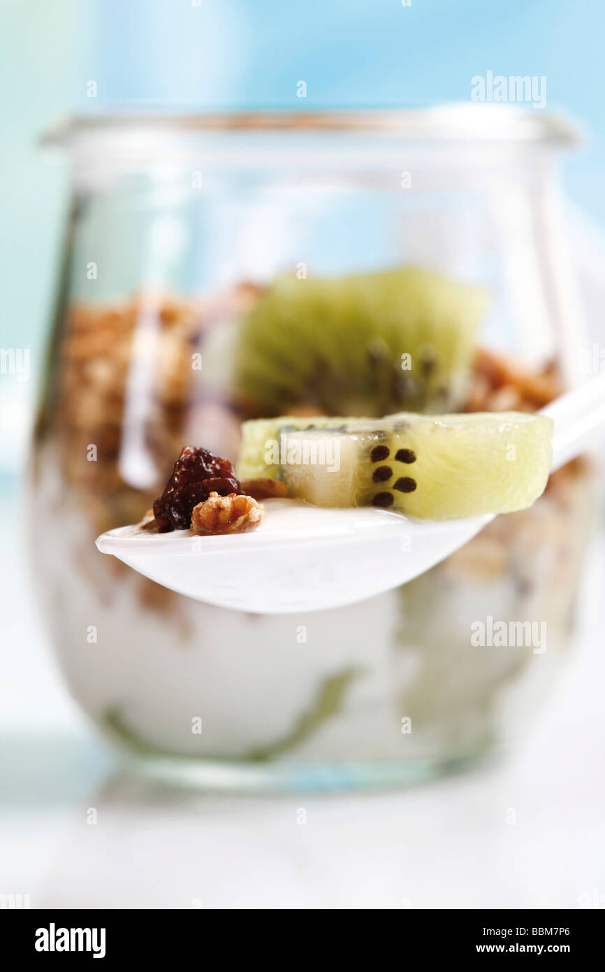 Muesli con yogur y kiwi en una pequeña jarra de cristal y una cuchara de yogur Foto de stock