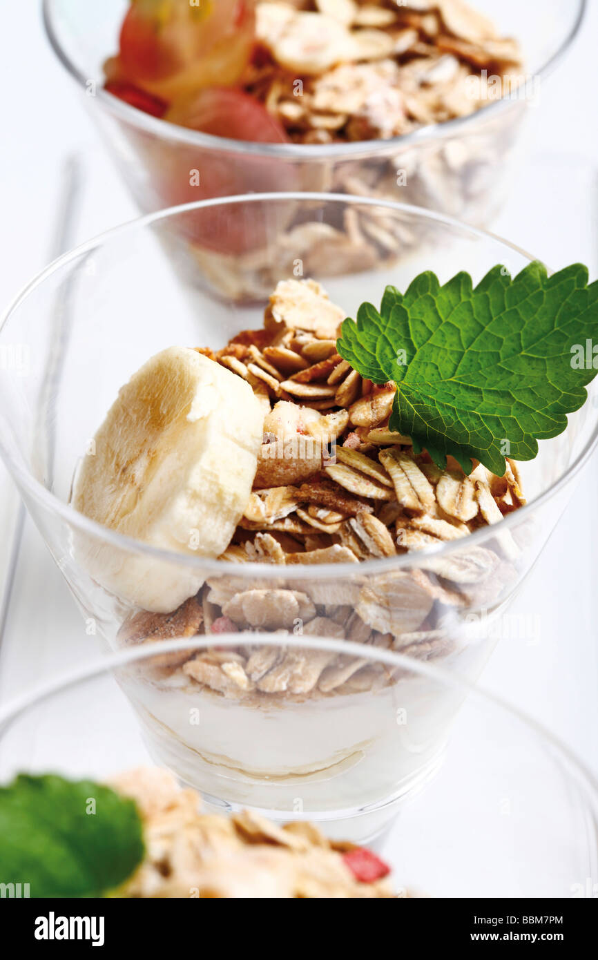 Muesli con yogur en un pequeño frasco de vidrio, rodajas de plátano, uvas, hojas de menta Foto de stock