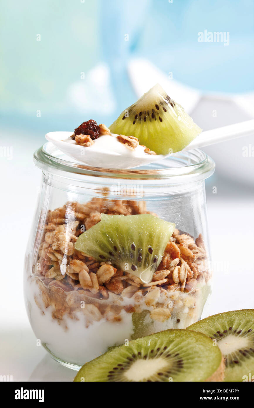 Muesli con yogur y kiwi en una pequeña jarra de cristal y una cuchara de yogur Foto de stock