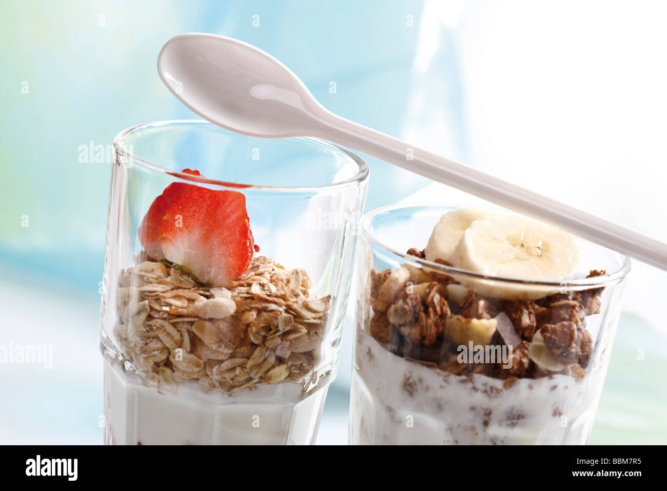 Muesli y chocolate muesli con yogur y en un pequeño frasco de vidrio, rodajas de plátano, fresas, yogurt cuchara Foto de stock