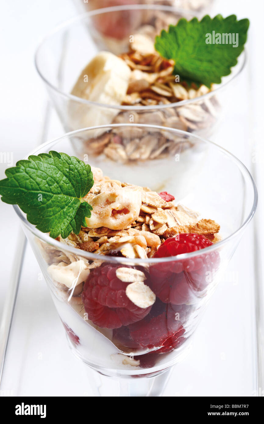 Muesli con yogur en un pequeño frasco de vidrio, rodajas de plátano, uvas, hojas de menta Foto de stock