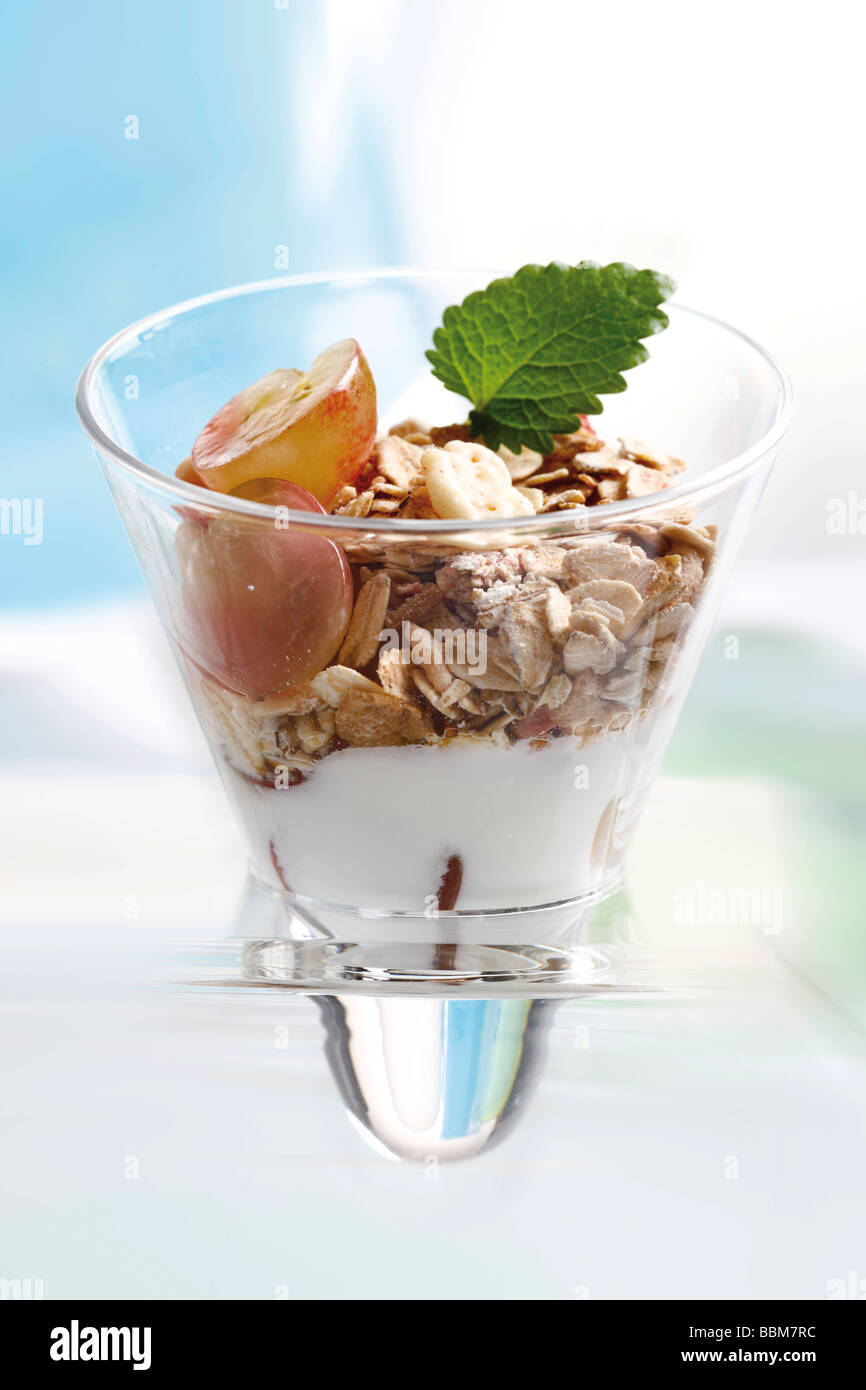 Muesli con yogur en un pequeño frasco de vidrio, uvas, hojas de menta Foto de stock