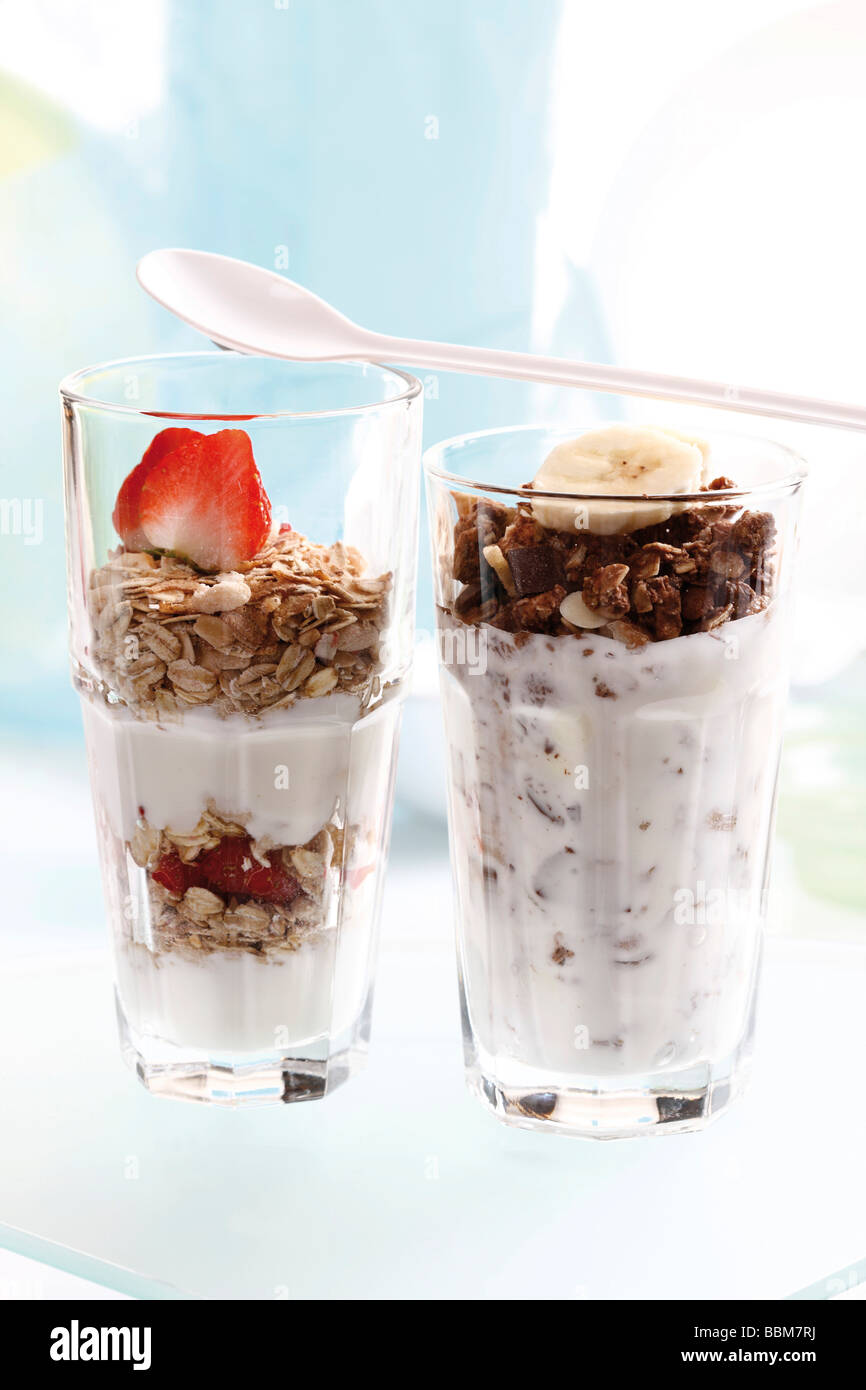 Muesli y chocolate muesli con yogur y en un pequeño frasco de vidrio, rodajas de plátano, fresas, yogurt cuchara Foto de stock