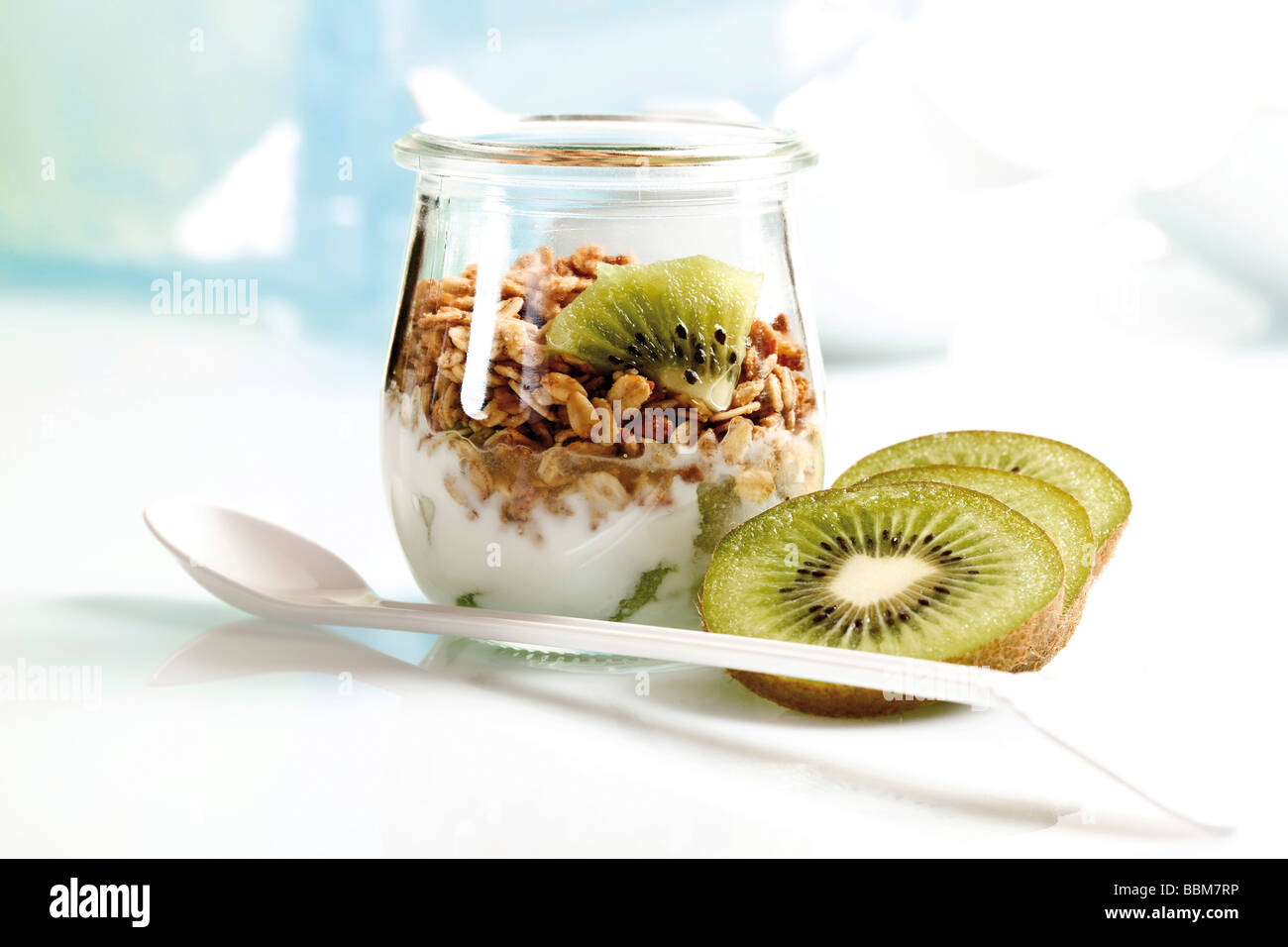Muesli con yogur y kiwi en una pequeña jarra de cristal y una cuchara de yogur Foto de stock