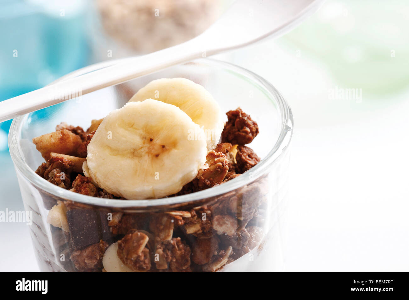 Chocolate muesli con yogur en un pequeño frasco de vidrio, rodajas de plátano, yogur cuchara Foto de stock