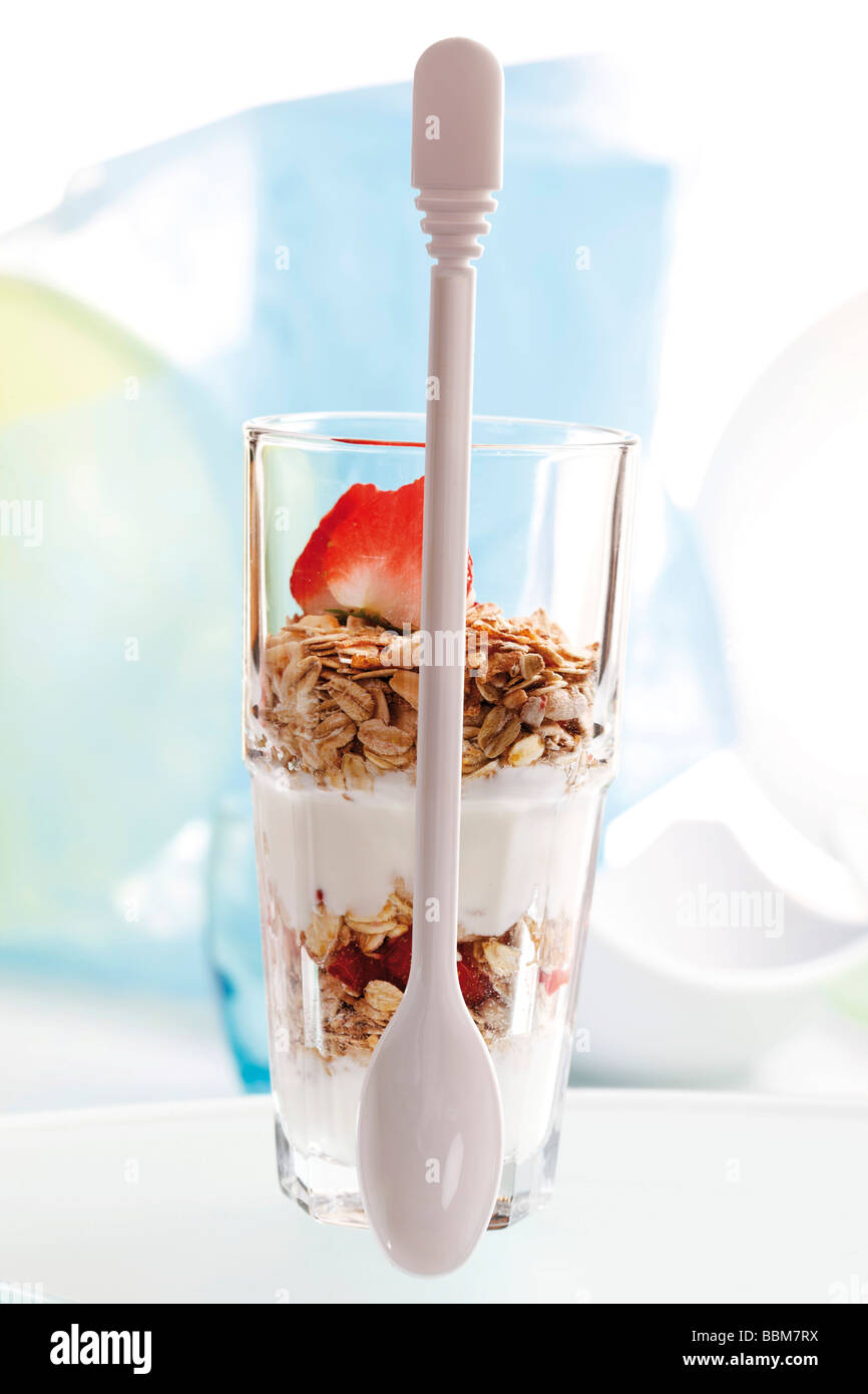 Muesli con yogur en un pequeño frasco de vidrio, fresas, yogurt cuchara Foto de stock