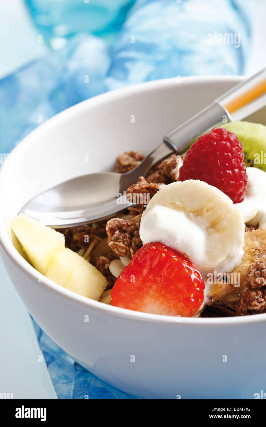 Muesli en un pequeño tazón de porcelana con yogur, fruta, caramelo quebradizo, frambuesas, fresas y uvas, kiwi, cuchara Foto de stock